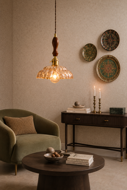 A warm, vintage-style pendant light with a textured amber glass shade and a dark wood finial hangs in a cozy, styled living room with a green armchair, round coffee table, and decorative wall plates.