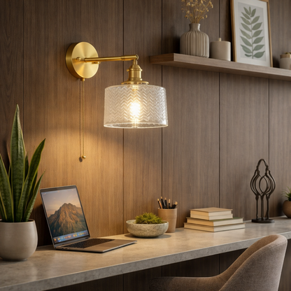 Elegant wall sconce with a clear, textured glass shade, complete with a pull chain switch and brass-finish base installed om study wall